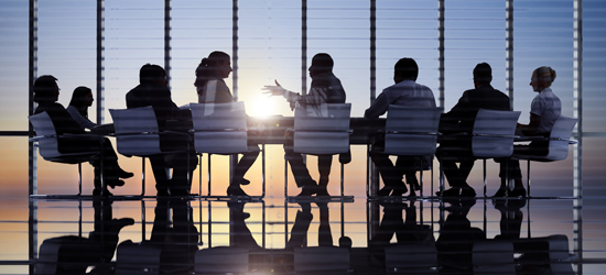 Employees meet in a large board room as the sun sets through the glassed wall