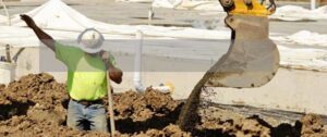 A construction worker gives a signal to a backhoe operator to release his bucket of dirt into a construction site