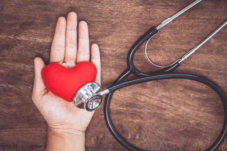 Red heart on woman's hand with doctor's stethoscope on wooden background