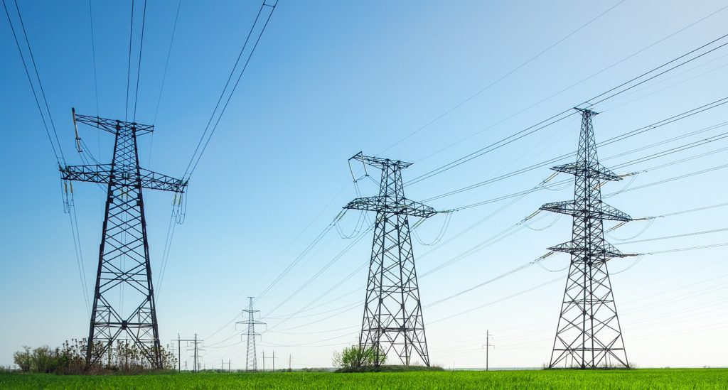 High voltage lines and power pylons in a green agricultural landscape with blue sky on a sunny day.