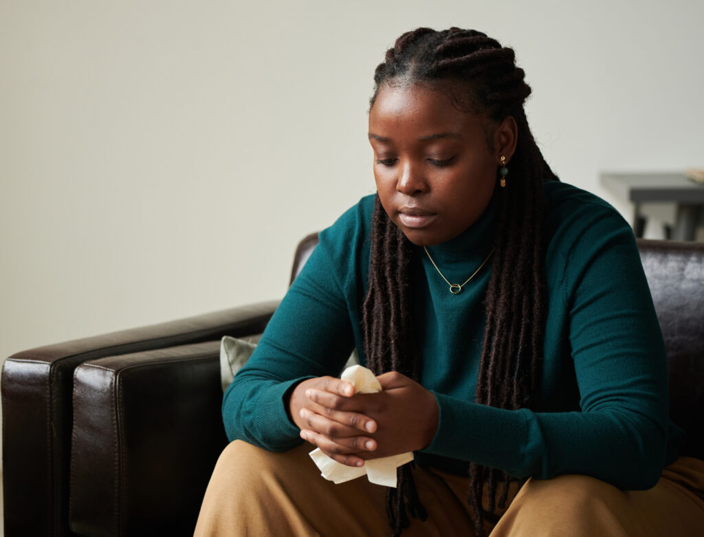 African American girl in depression sitting on sofa and holding tissues, she visiting psychologist at office