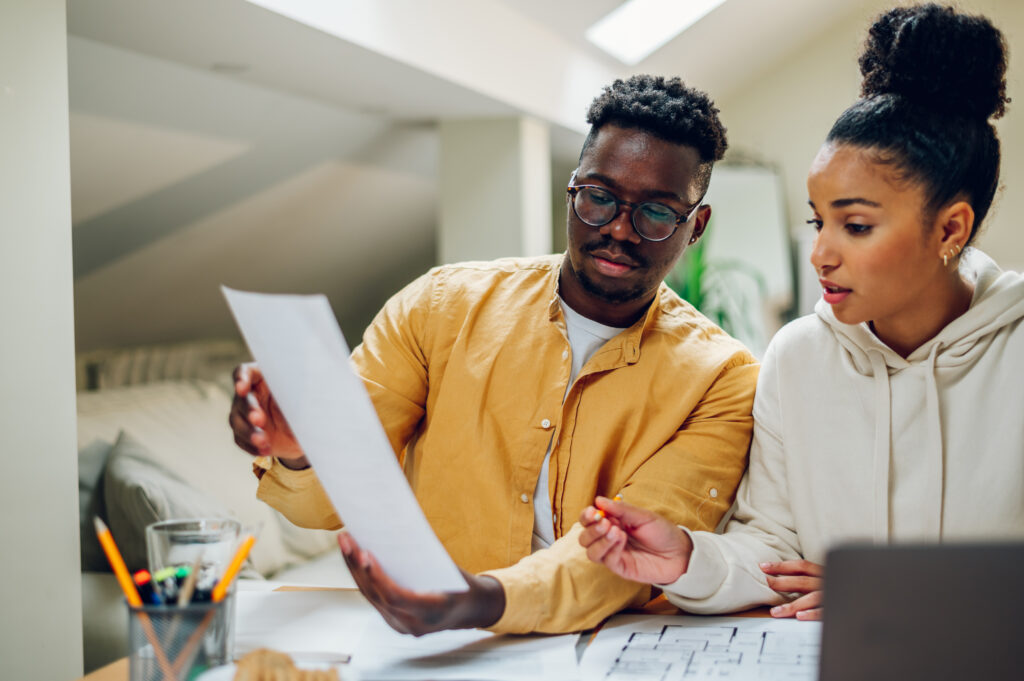 Multiracial couple looking into the blueprints of their future home and making a financial plan for that investment. Romantic diverse couple working together at home. Redecorating and relocation.