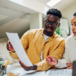 Multiracial couple looking into the blueprints of their future home and making a financial plan for that investment. Romantic diverse couple working together at home. Redecorating and relocation.