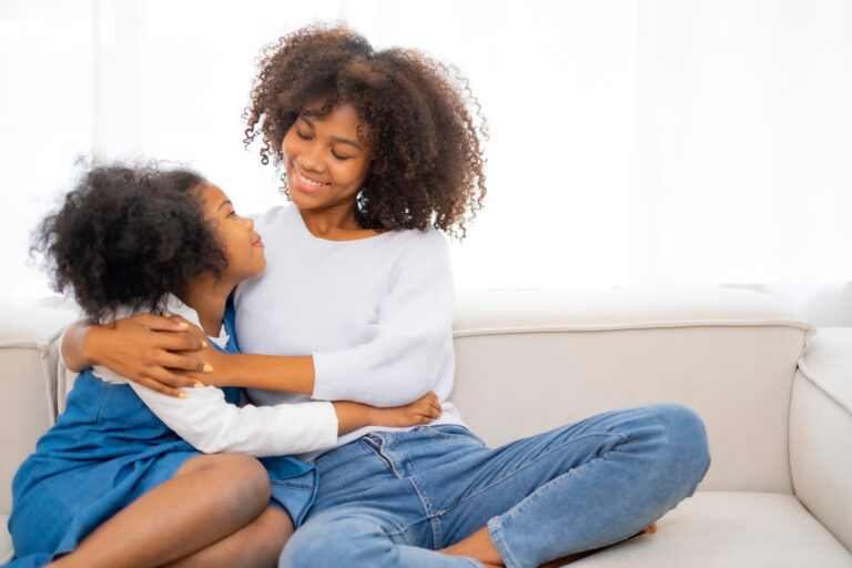African American young mother embrass her daughter with smile of love, looking each other on sofa at home, Black couple woman and kid express feelling of love.