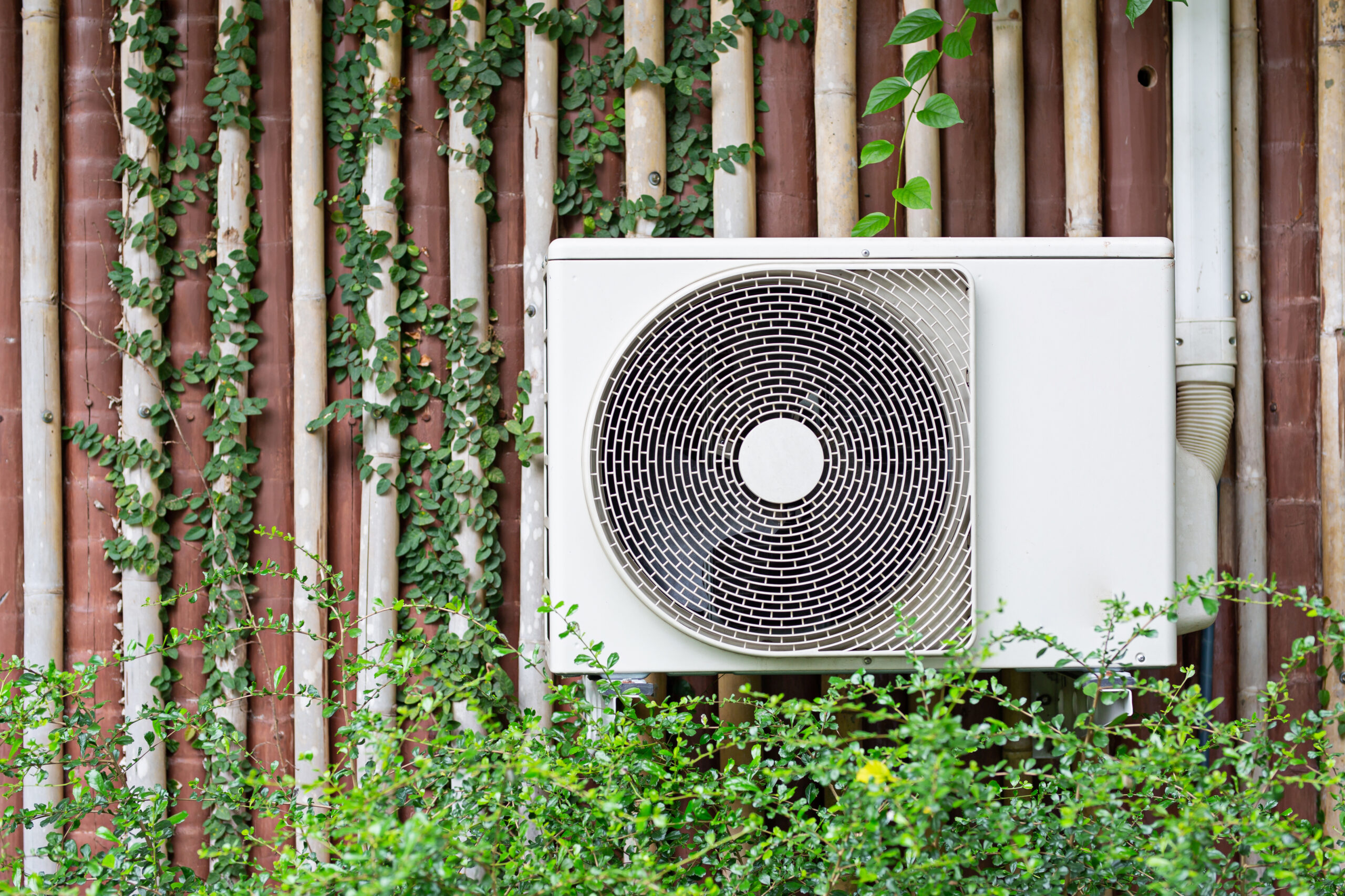 The air conditioner is mounted on the wall with the trees of the building with the garden in the front row.