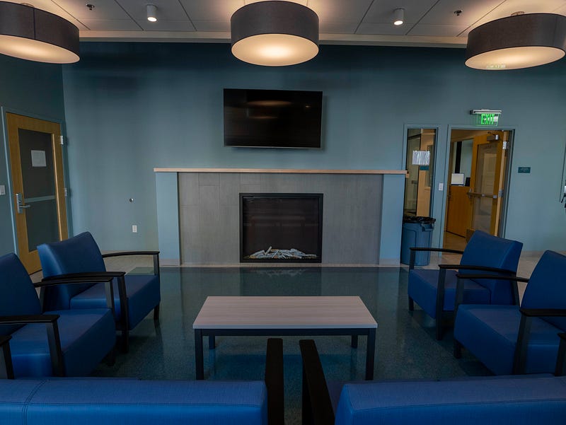 A community space inside Plymouth's Blake House has a fireplace, television, and six blue chairs arranged in a u-shape around a coffee table. 