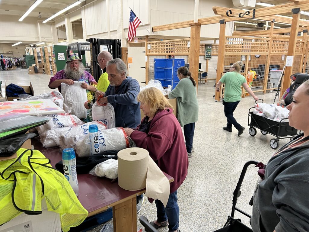 Five of The Moore Wright Group staff members work together to place blankets in bags inside the organization's warehouse location. Two other staff members are working in the background.