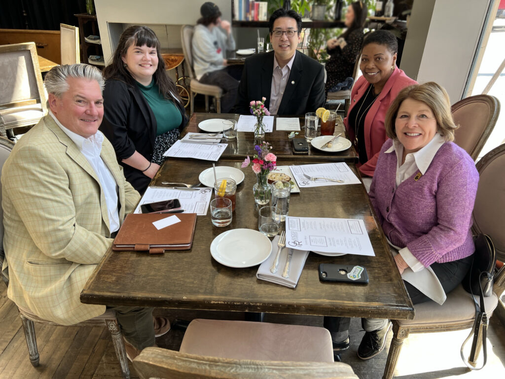Five people pose while sitting around a restaurant table with menus.