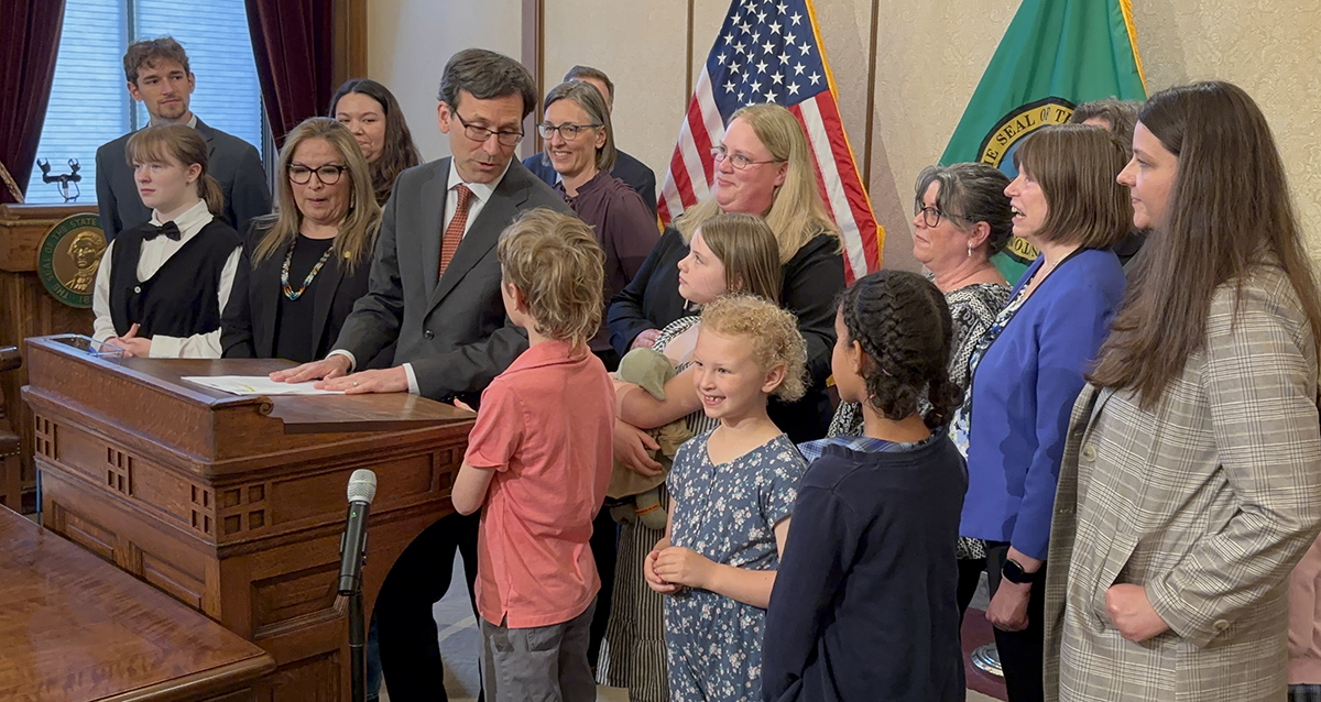 Commerce employees and their children, as well as bill sponsor State Senator Claudia Kauffman, join Gov. Bob Ferguson at the bill signing.